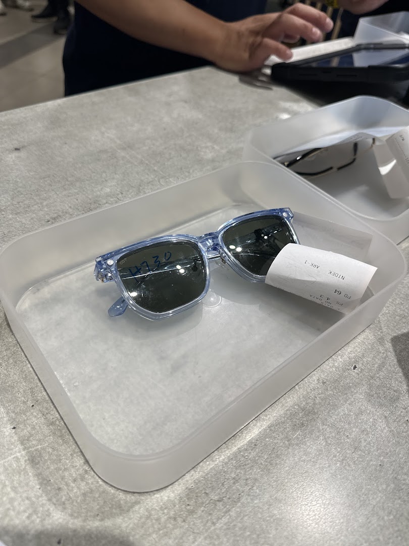 A pair of light blue sunglasses in a tray on a counter, with a person's hands in the background.