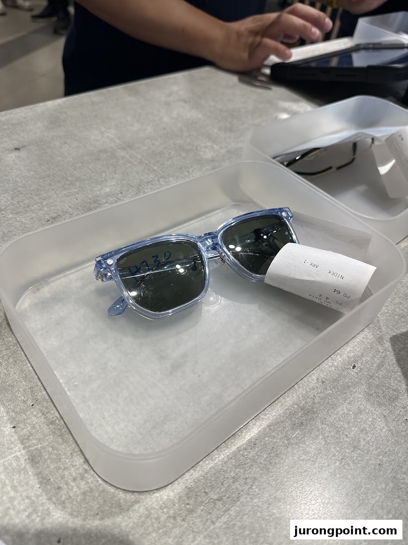 A pair of light blue sunglasses in a tray on a counter, with a person's hands in the background.