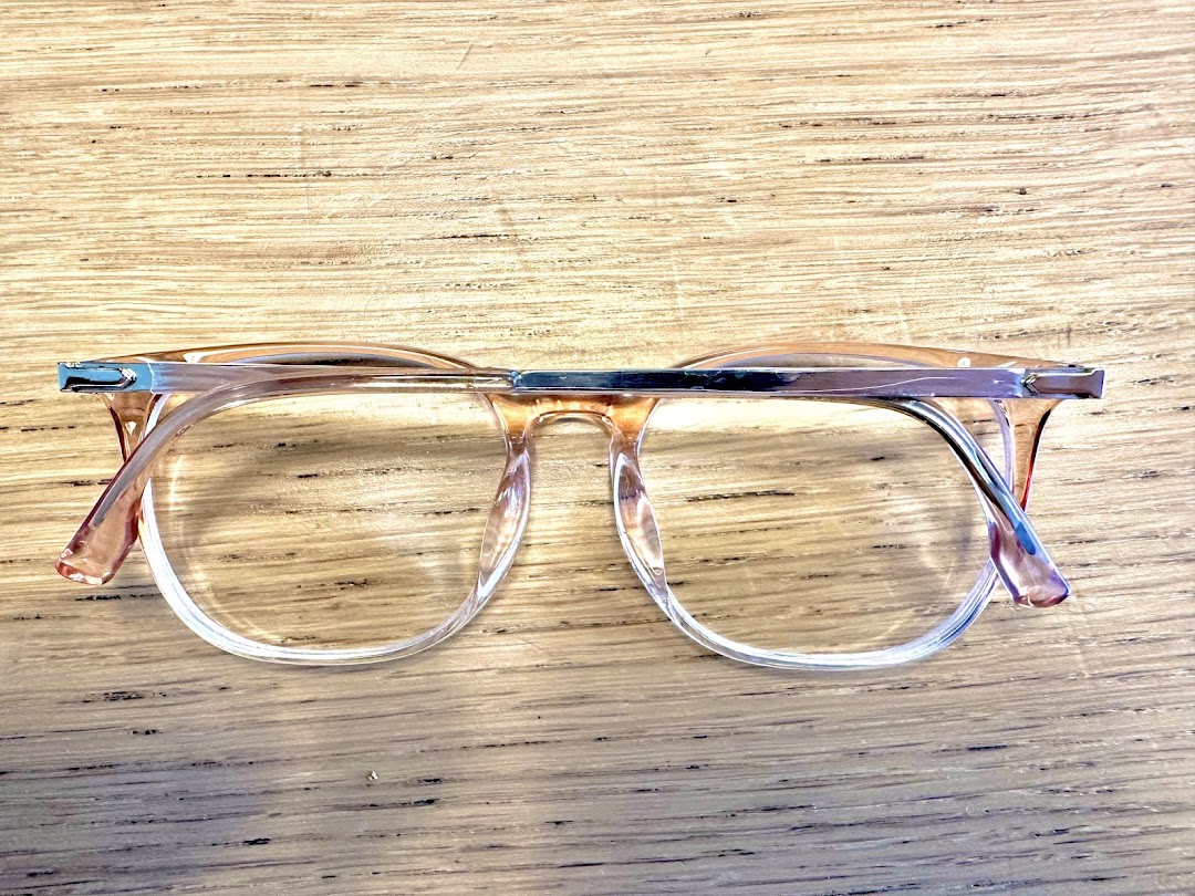 A pair of stylish clear-framed eyeglasses rests on a wooden surface.