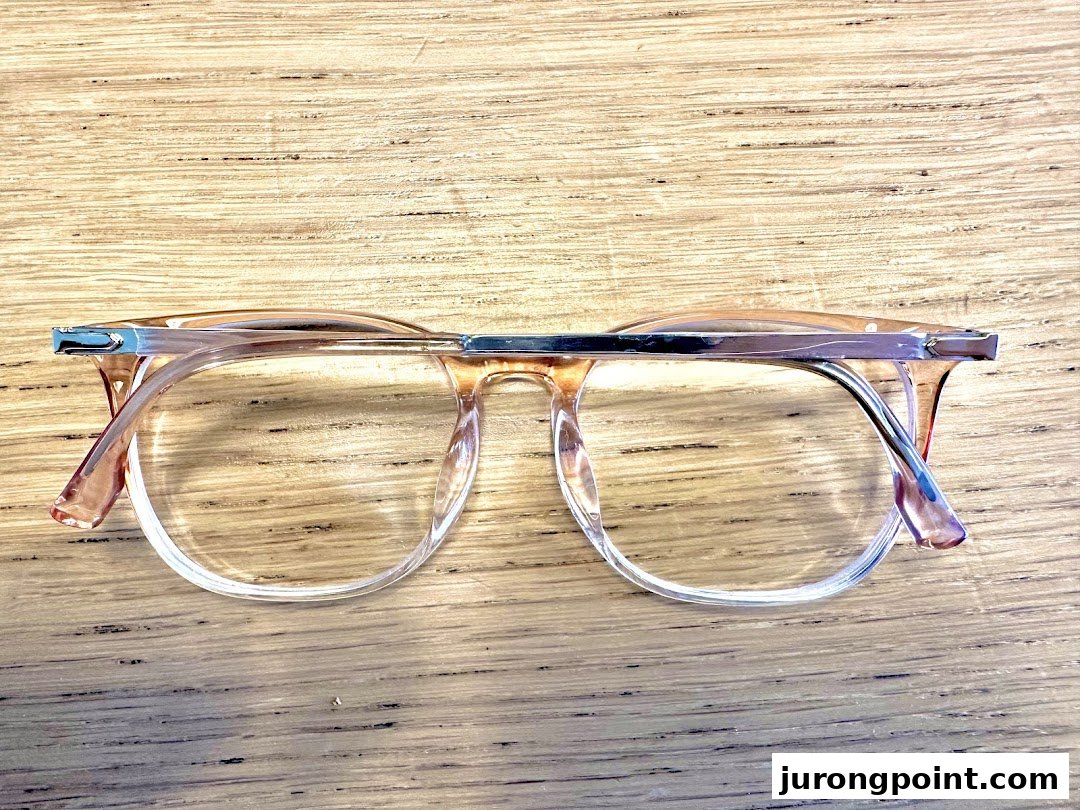 A pair of stylish clear-framed eyeglasses rests on a wooden surface.