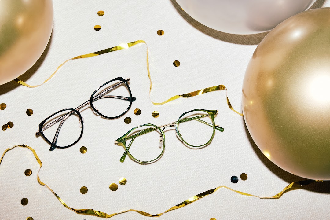 Two stylish pairs of eyeglasses are displayed amidst golden confetti and balloons on a white surface.
