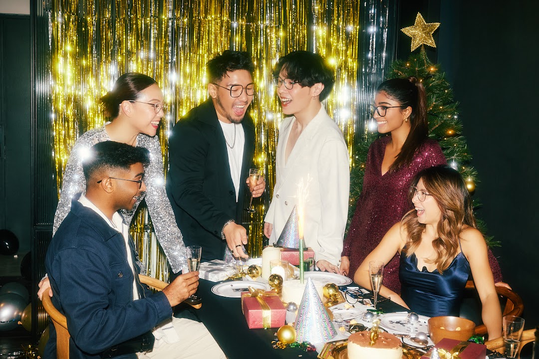 A diverse group of friends wearing stylish eyewear celebrates joyfully at a festive party with cake and champagne.