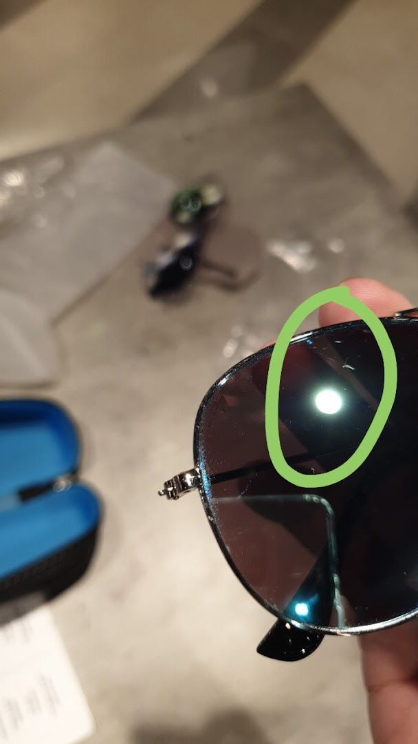 Close-up of sunglasses held in hand, showing a reflection, with a case and other items in the background.