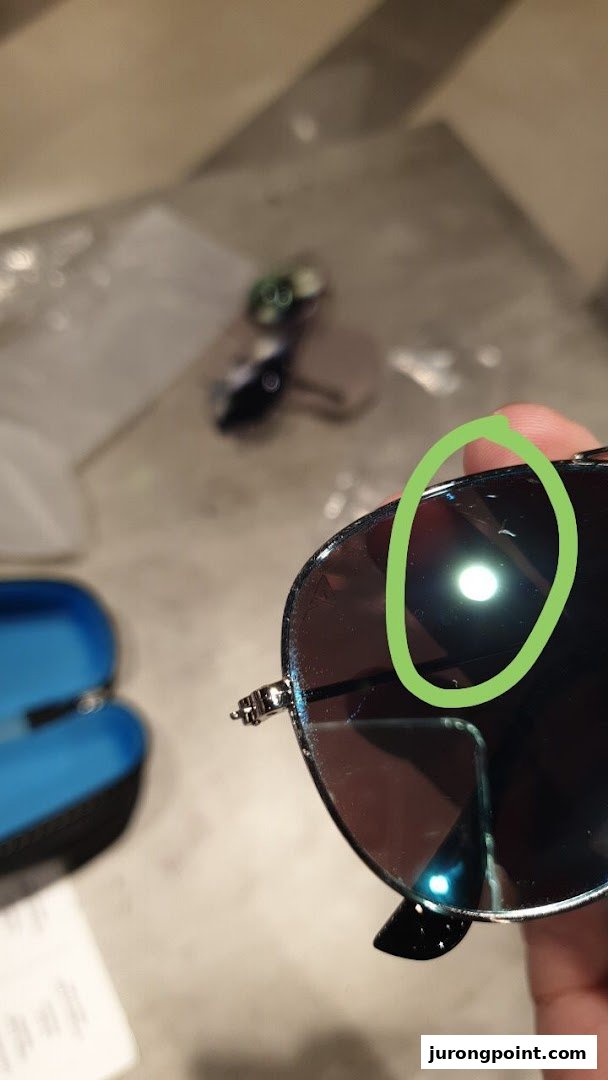 Close-up of sunglasses held in hand, showing a reflection, with a case and other items in the background.