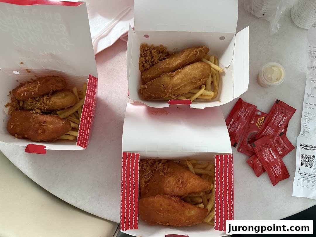 Three open boxes of Long John Silver's fried fish and chips with sauces on a table.