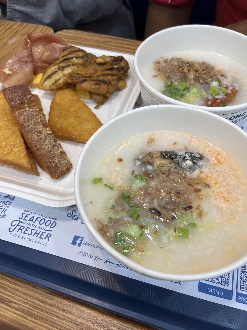A tray of diverse breakfast items including congee, grilled chicken, hash browns, and fried toast.