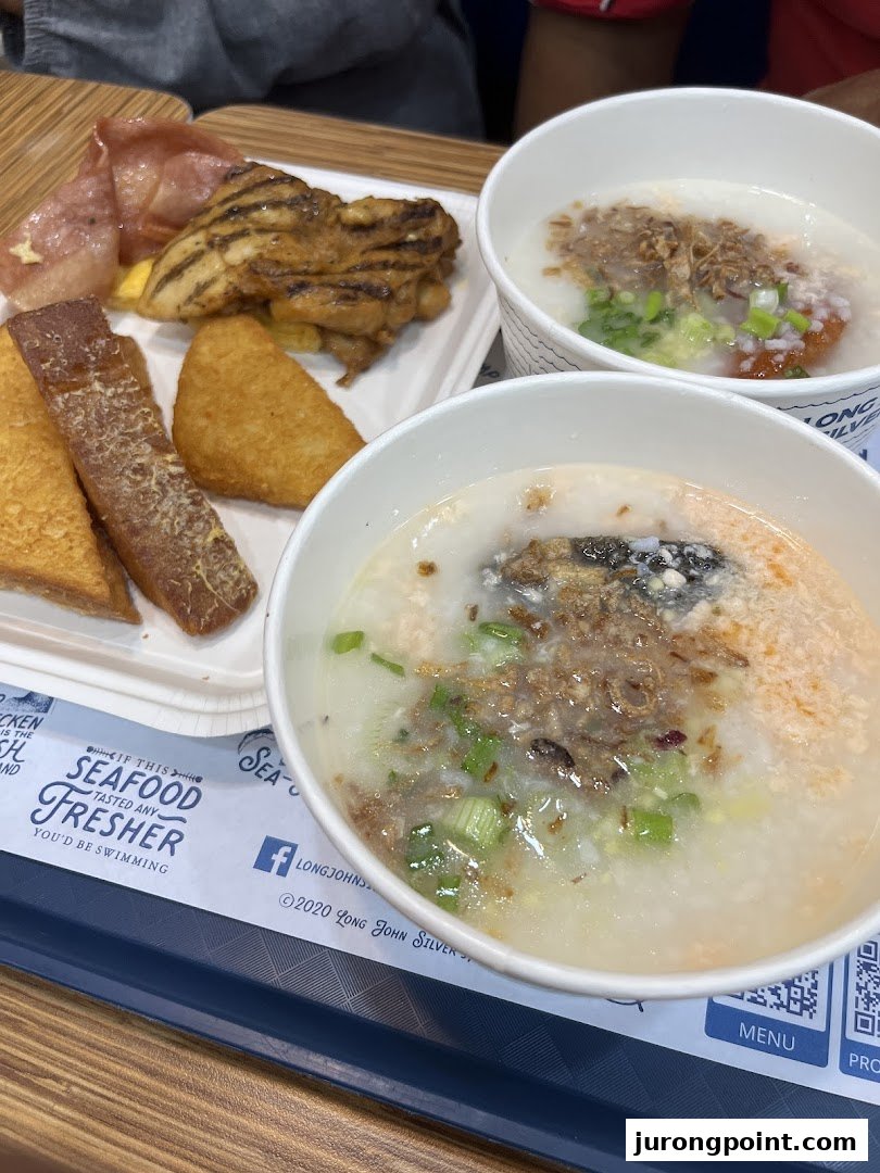 A tray of diverse breakfast items including congee, grilled chicken, hash browns, and fried toast.