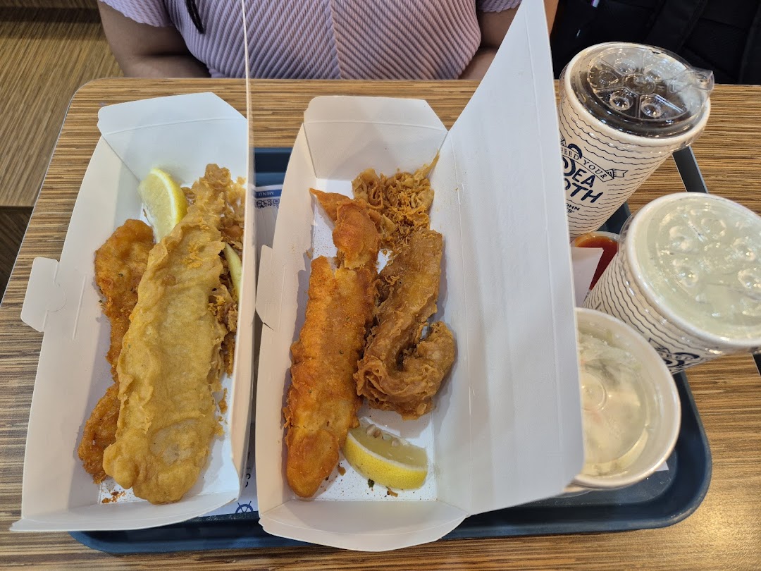A tray with two boxes of crispy fried fish and seafood, accompanied by drinks and coleslaw.