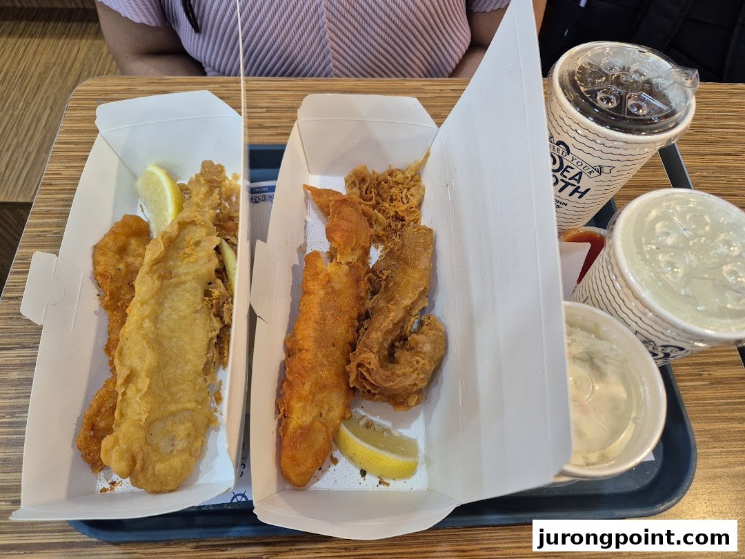 A tray with two boxes of crispy fried fish and seafood, accompanied by drinks and coleslaw.