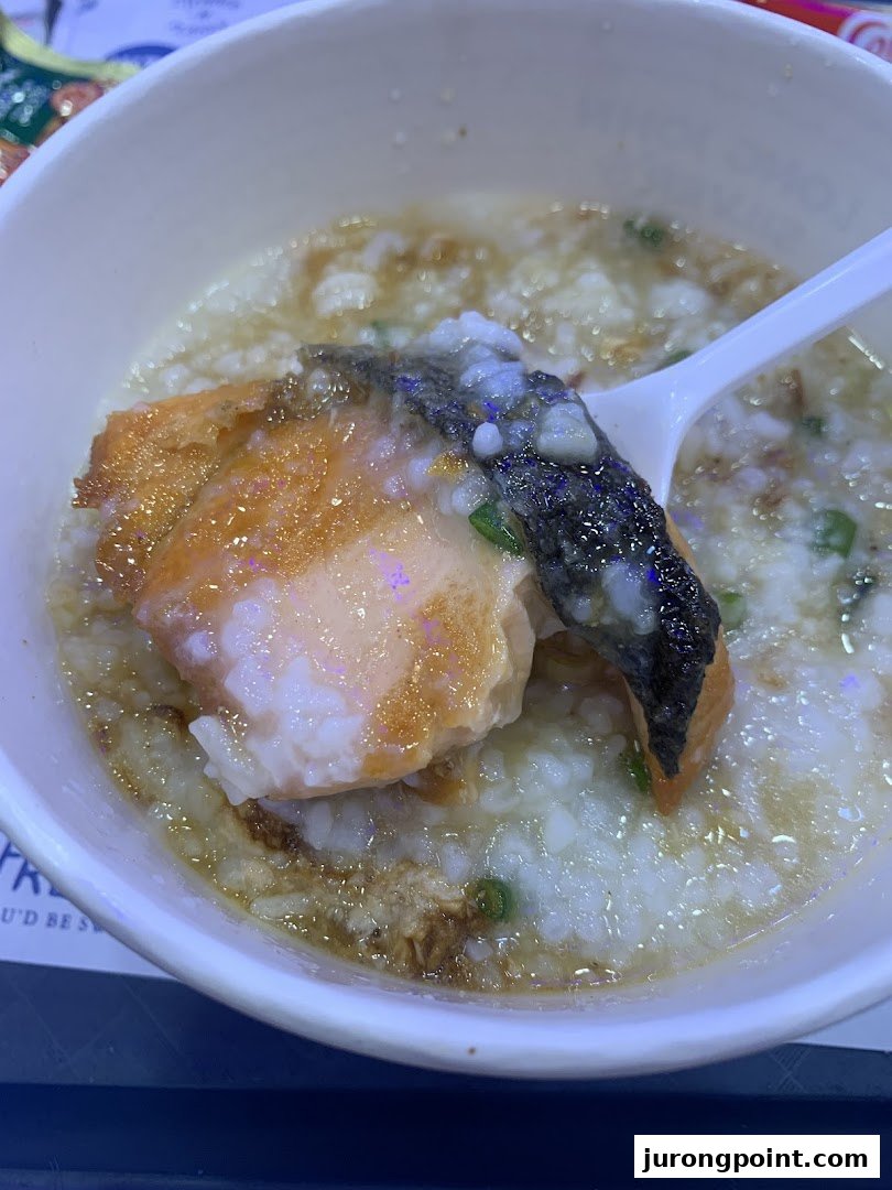 A close-up of a comforting bowl of congee topped with a large piece of savory salmon.