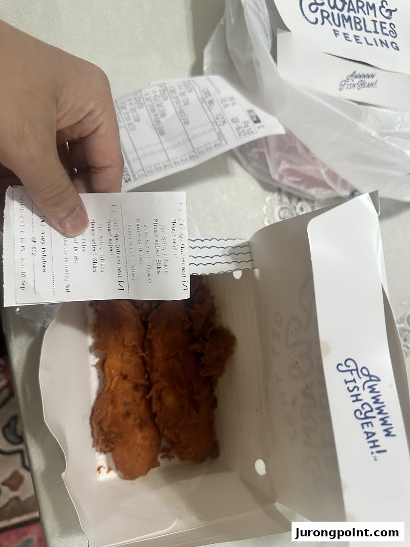 A hand holds a receipt over a box containing crispy fried chicken from Long John Silver's.