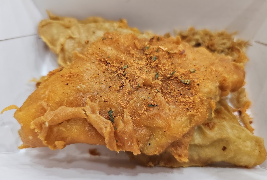 Close-up of golden-brown battered fish or seafood, seasoned with spices, in a white container.