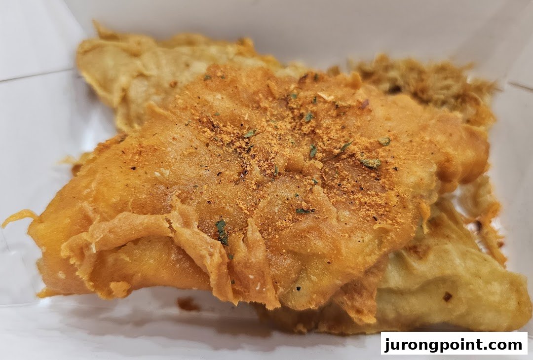 Close-up of golden-brown battered fish or seafood, seasoned with spices, in a white container.