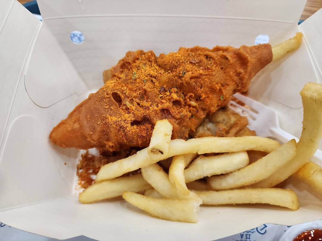 A close-up of crispy, seasoned fried fish and golden french fries in a takeout box.