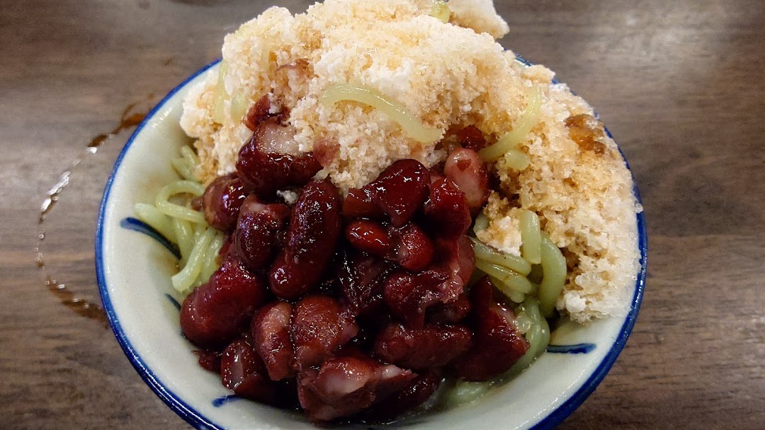 A close-up of a refreshing bowl of Cendol with green jelly noodles, red beans, and shaved ice.