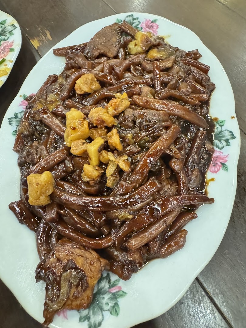 A close-up of a plate of dark, saucy Hokkien Mee noodles with meat and crispy pork lard.
