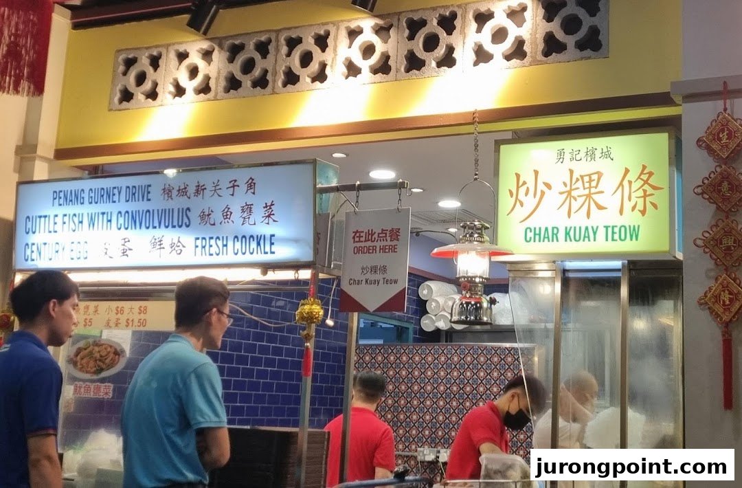A bustling food stall counter featuring signs for Char Kuay Teow and other Malaysian dishes.