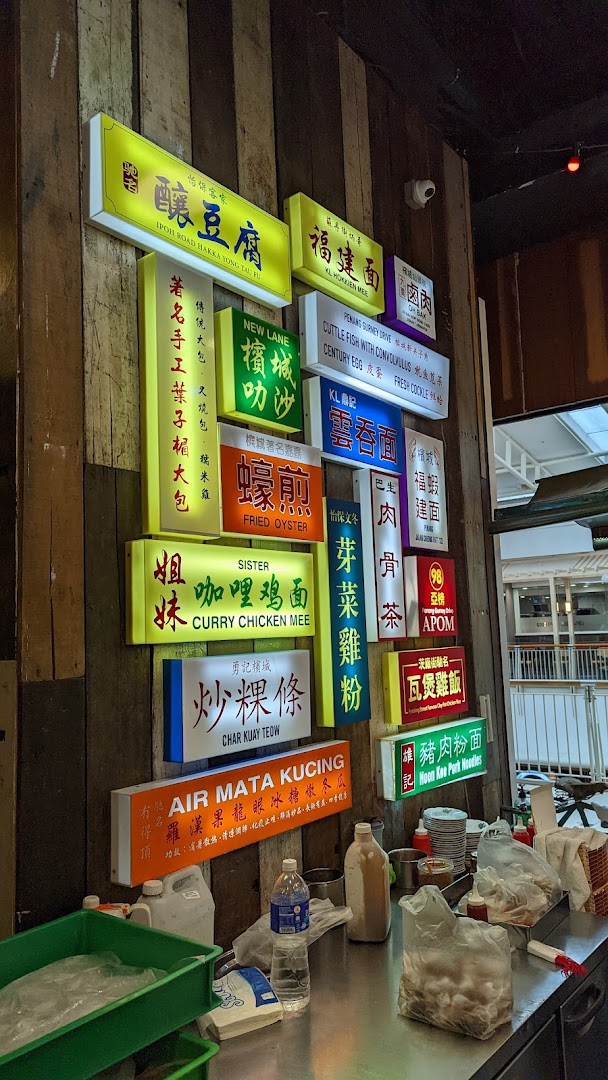 A vibrant wall display featuring numerous illuminated signs advertising diverse Malaysian hawker dishes and drinks.