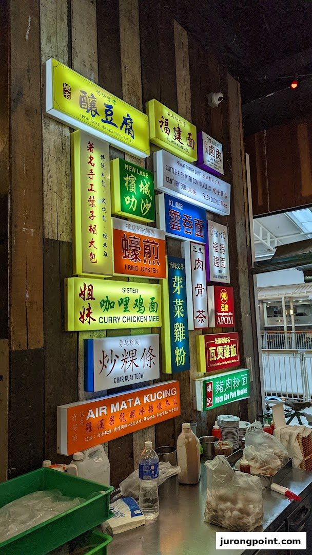 A vibrant wall display featuring numerous illuminated signs advertising diverse Malaysian hawker dishes and drinks.