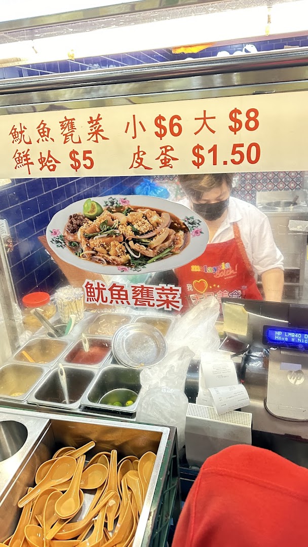 A food stall counter featuring a menu board with prices and a staff member preparing food.