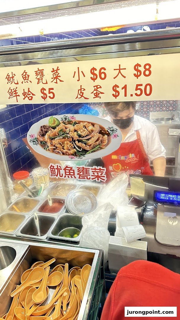A food stall counter featuring a menu board with prices and a staff member preparing food.