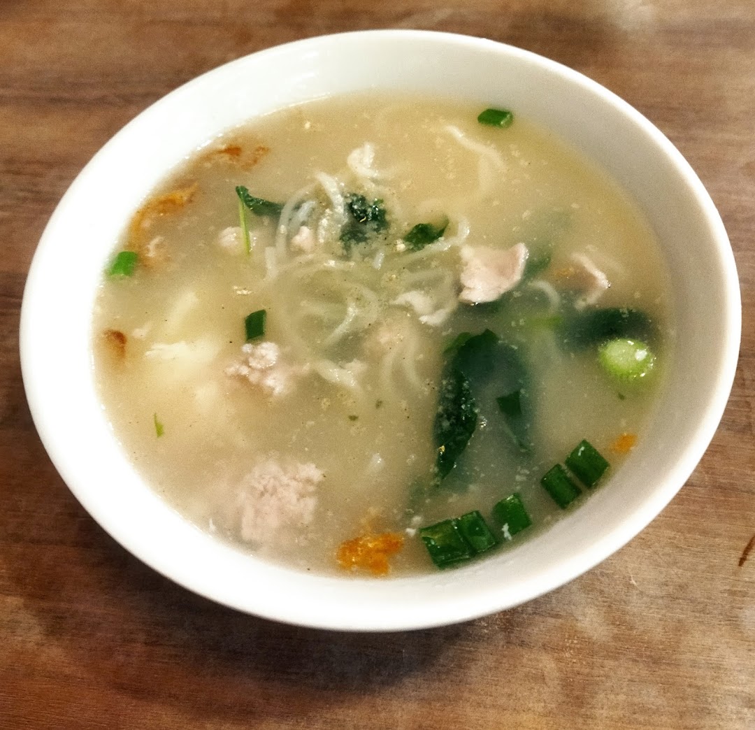 A close-up of a hearty bowl of clear noodle soup with minced meat, greens, and spring onions.