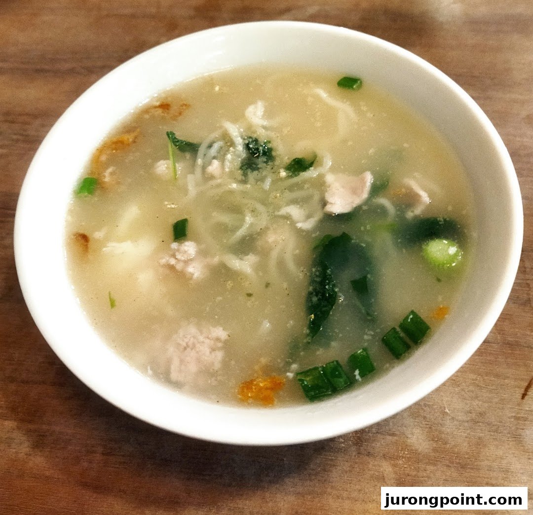 A close-up of a hearty bowl of clear noodle soup with minced meat, greens, and spring onions.