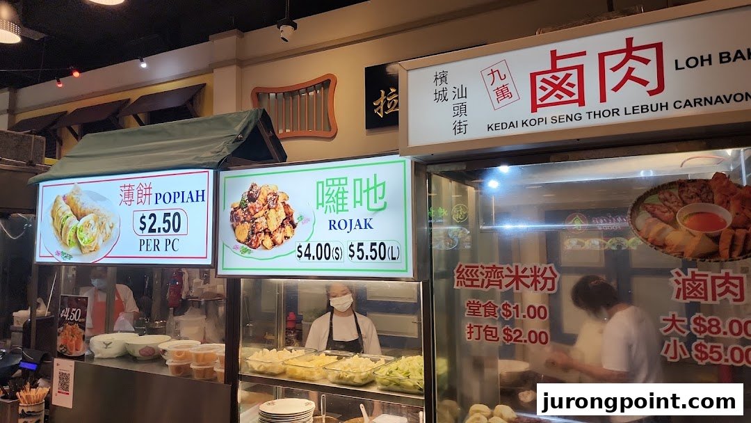 A vibrant food stall display showcasing various Malaysian hawker dishes with prices and descriptions.