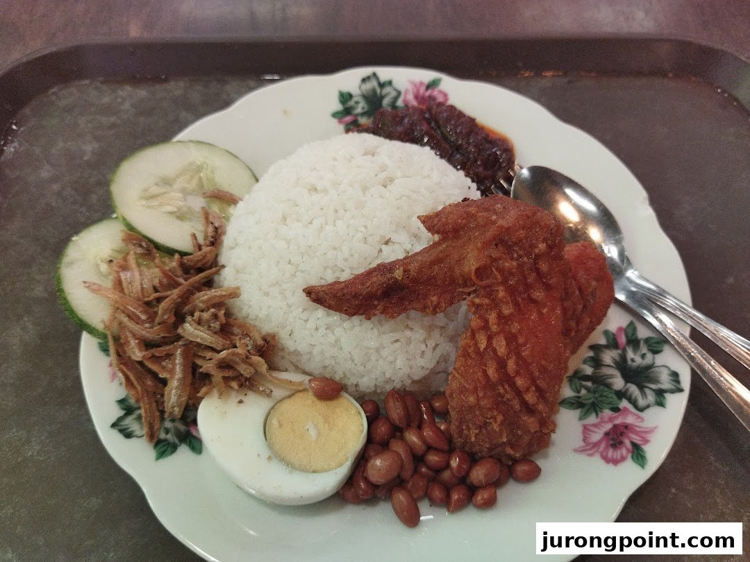 A delicious plate of Nasi Lemak with fried chicken, anchovies, peanuts, egg, and cucumber.