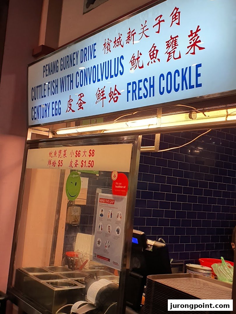 A food stall counter displaying a menu board with Penang-style dishes and prices.
