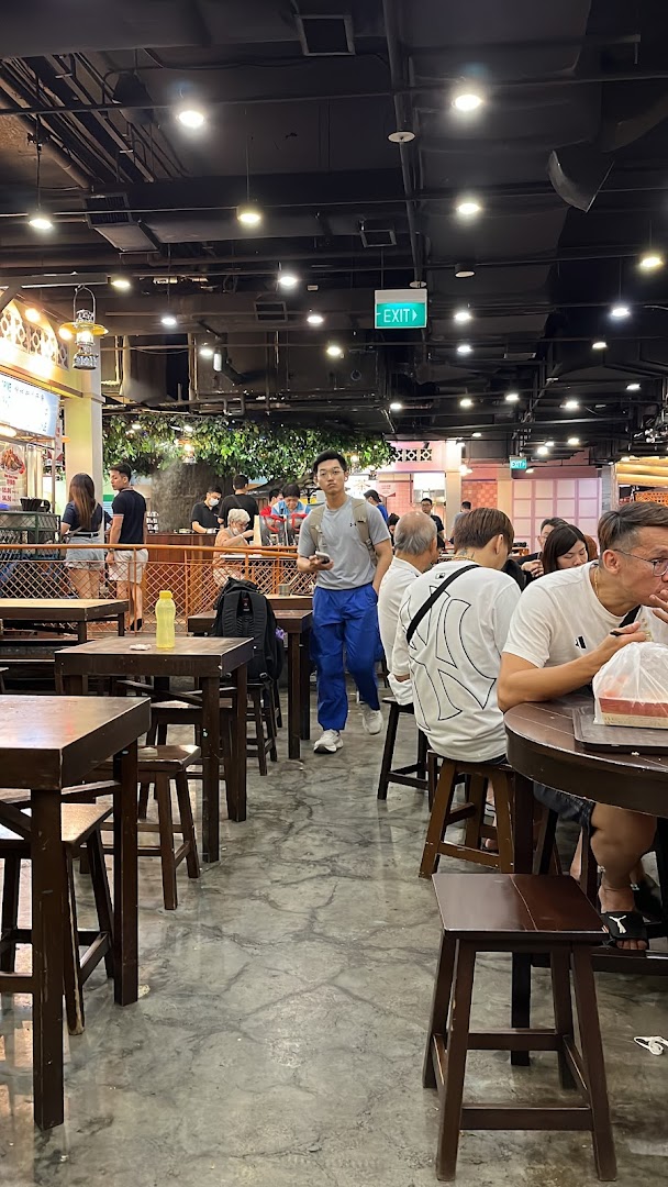 Diners and a man walking through a bustling food court with wooden tables and stools.
