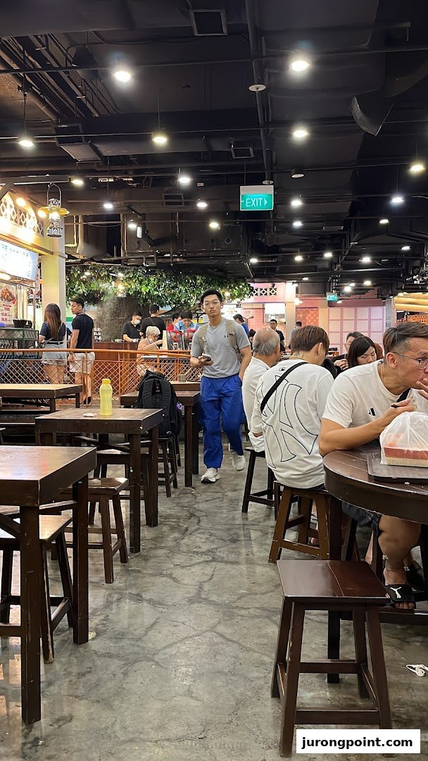 Diners and a man walking through a bustling food court with wooden tables and stools.