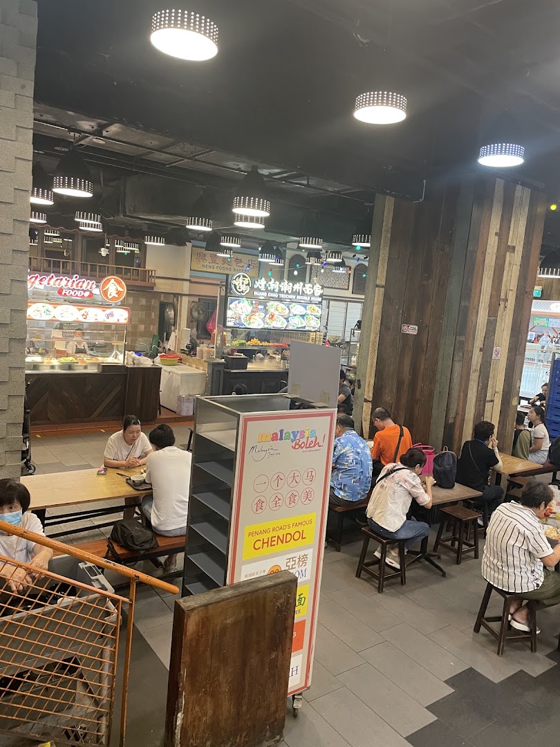 A lively food court interior at Malaysia Boleh! with various food stalls and diners enjoying meals.