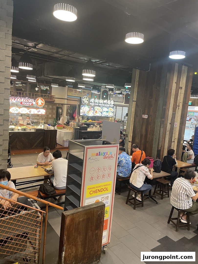 A lively food court interior at Malaysia Boleh! with various food stalls and diners enjoying meals.