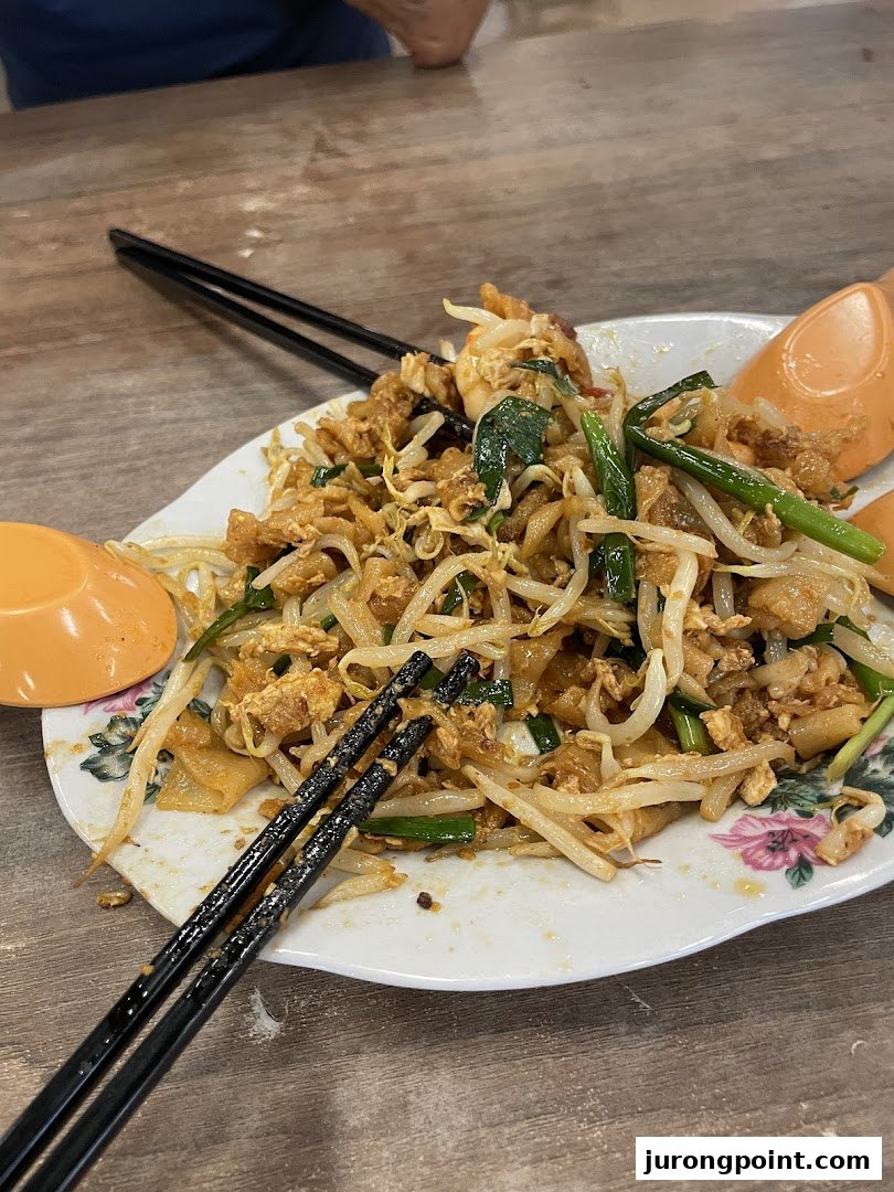 A close-up of a delicious plate of stir-fried noodles with bean sprouts and eggs, served with chopsticks.