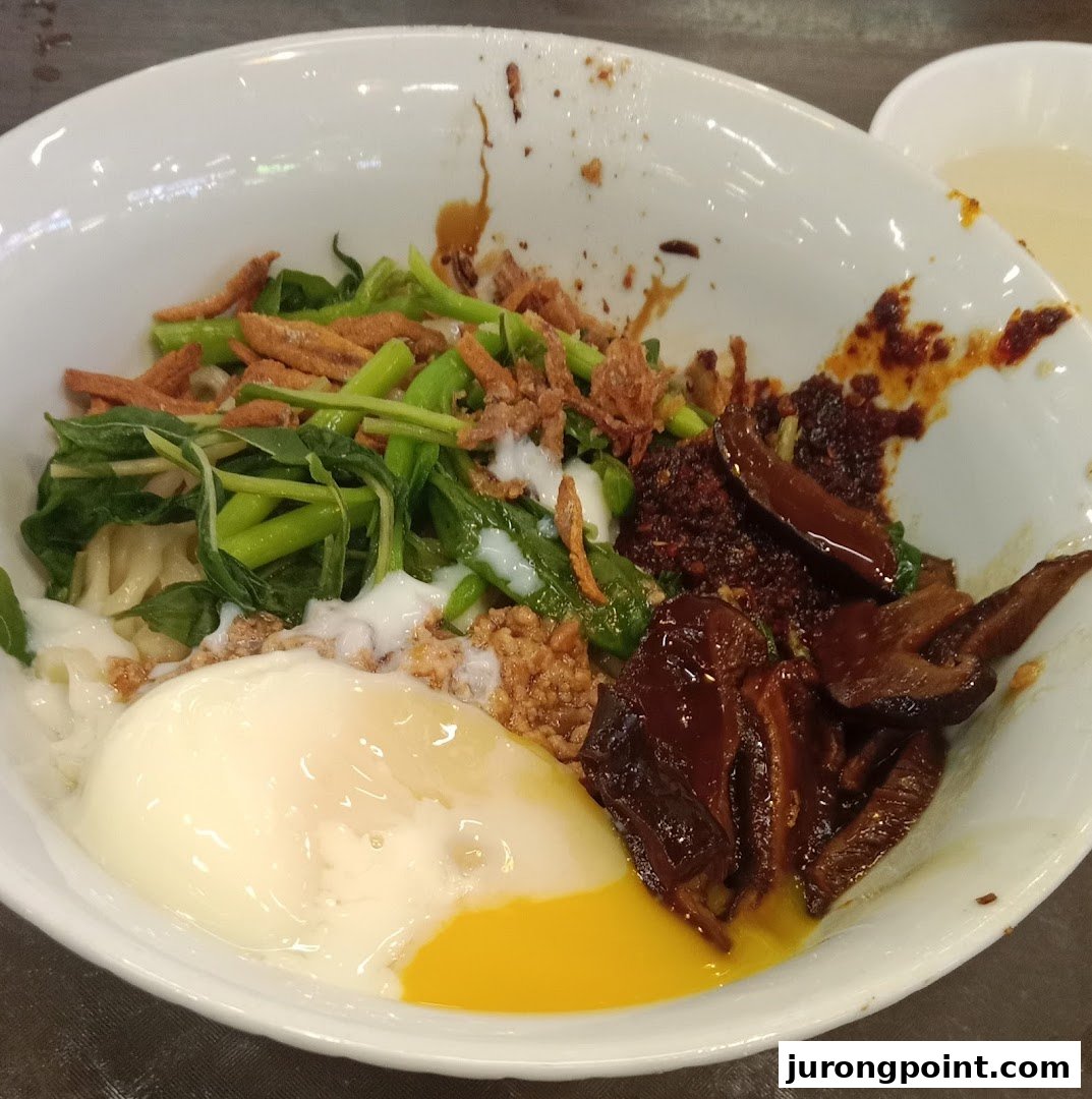A vibrant bowl of Malaysian noodles with a runny egg, greens, mushrooms, and chili.