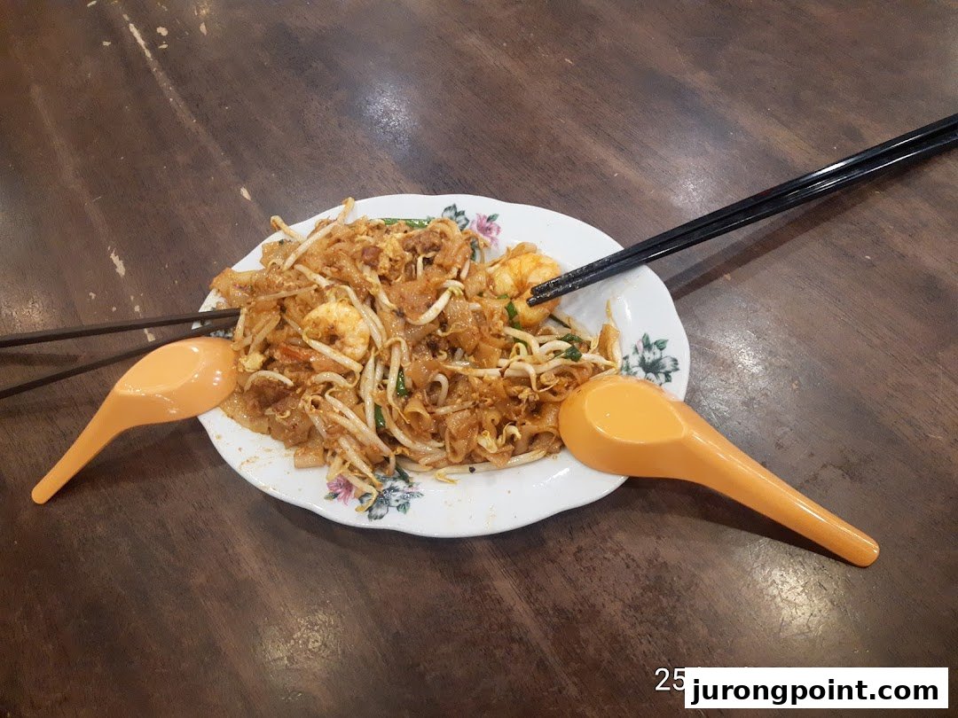 A delicious plate of Char Kway Teow with prawns and bean sprouts on a wooden table.