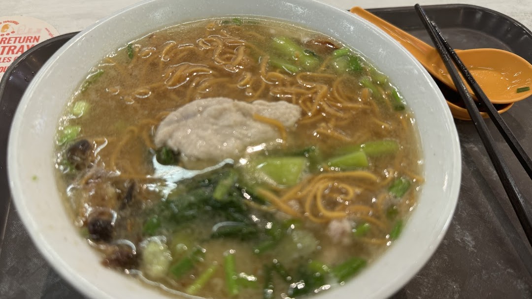 A close-up of a delicious bowl of noodles with broth, vegetables, and a large meatball.