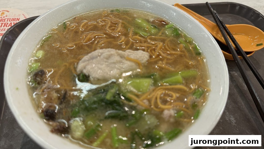 A close-up of a delicious bowl of noodles with broth, vegetables, and a large meatball.