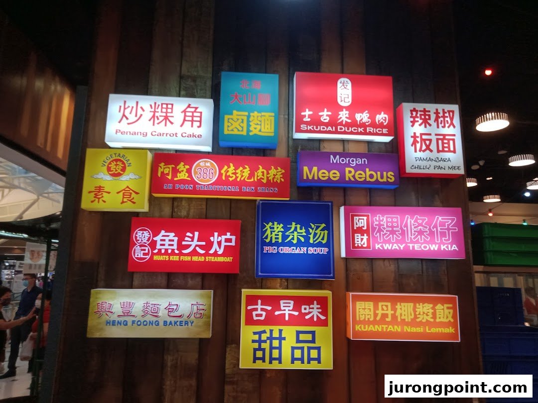 Illuminated signs on a wooden wall showcasing a variety of Malaysian food stalls and dishes.