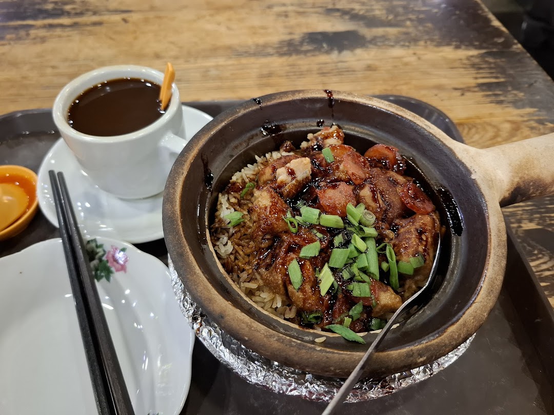 A delicious claypot rice dish with meat and a cup of coffee on a wooden table.