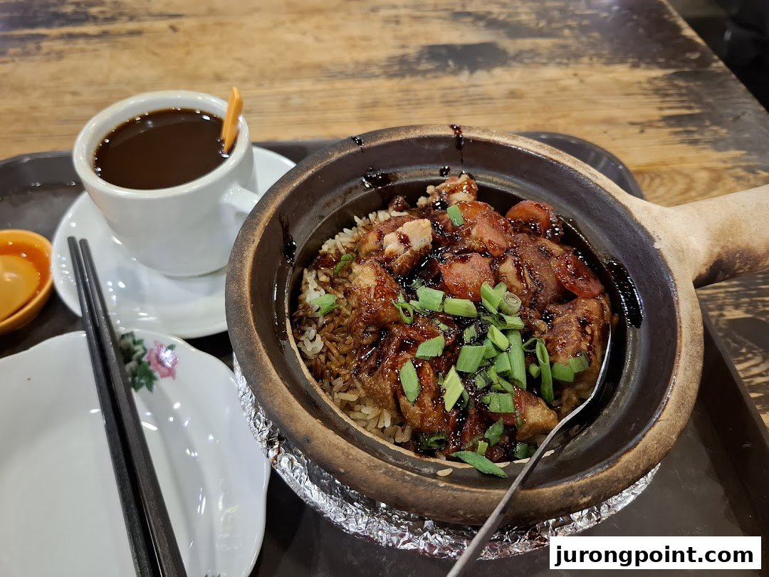 A delicious claypot rice dish with meat and a cup of coffee on a wooden table.