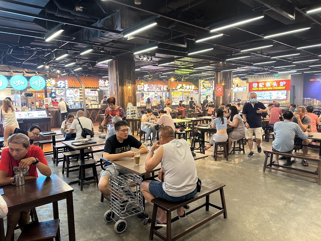 A lively food court filled with patrons enjoying diverse Malaysian cuisine at various stalls.