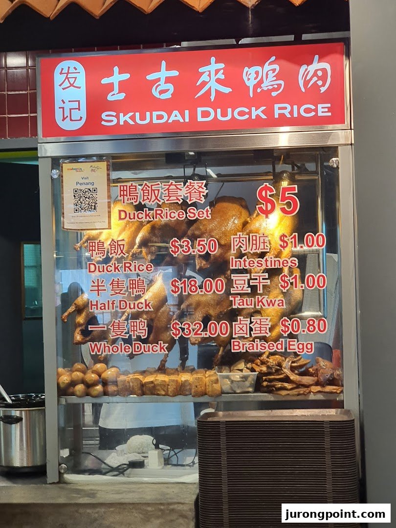 A food stall display featuring roasted ducks and a menu with prices for duck rice and side dishes.