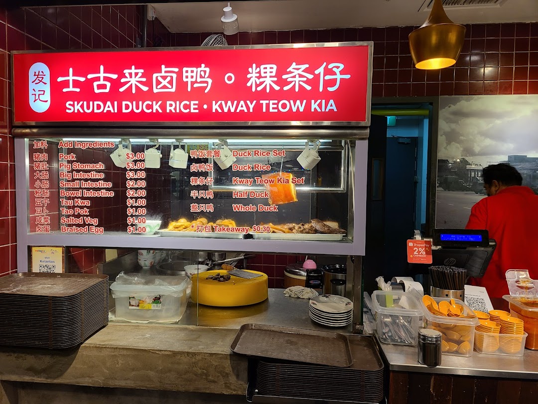 A bustling food stall counter featuring a menu board for duck rice and kway teow.