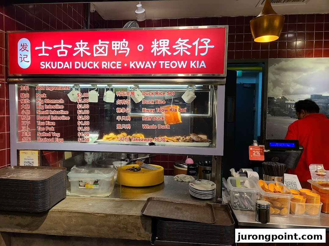 A bustling food stall counter featuring a menu board for duck rice and kway teow.