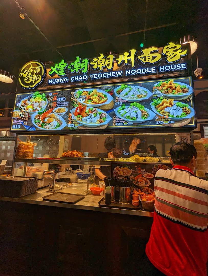 A vibrant food stall counter with a large illuminated menu board showcasing various Teochew noodle dishes.