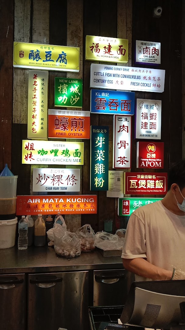 An indoor food stall counter with numerous illuminated signs displaying various Malaysian dishes.