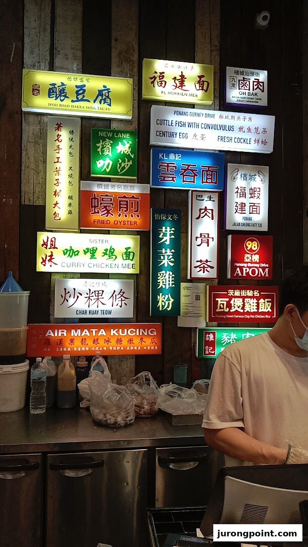 An indoor food stall counter with numerous illuminated signs displaying various Malaysian dishes.