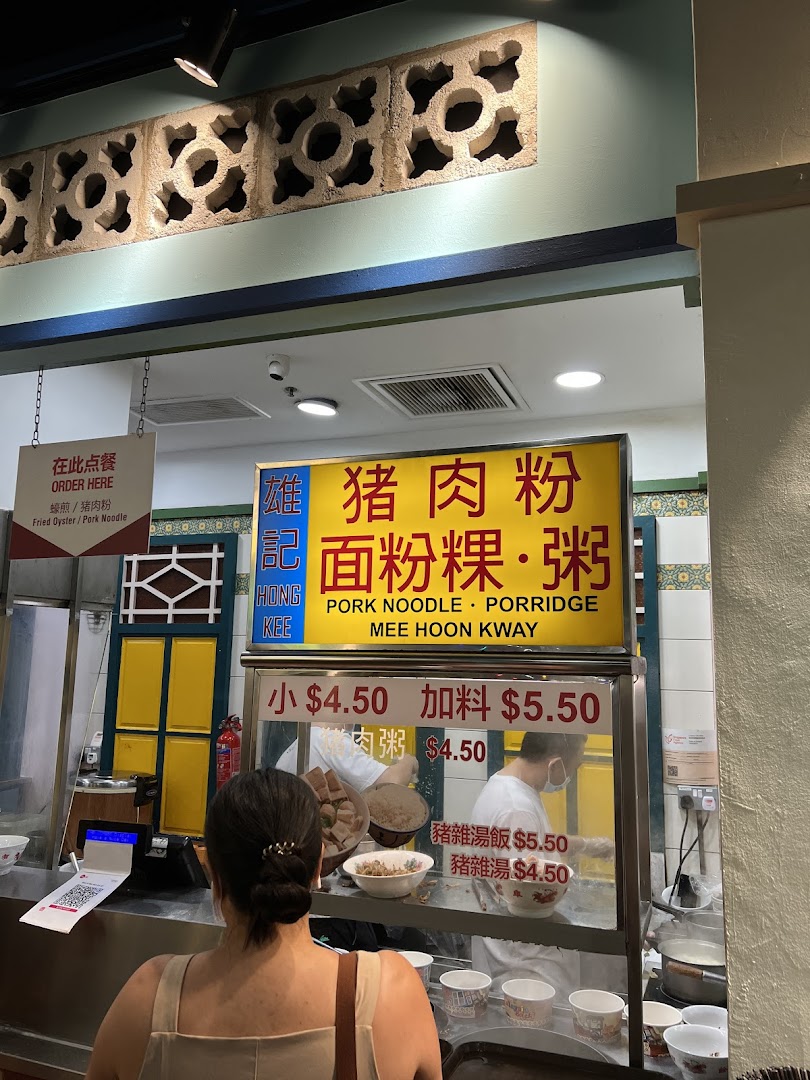 A customer at a food stall counter with a menu board displaying pork noodle and porridge options.